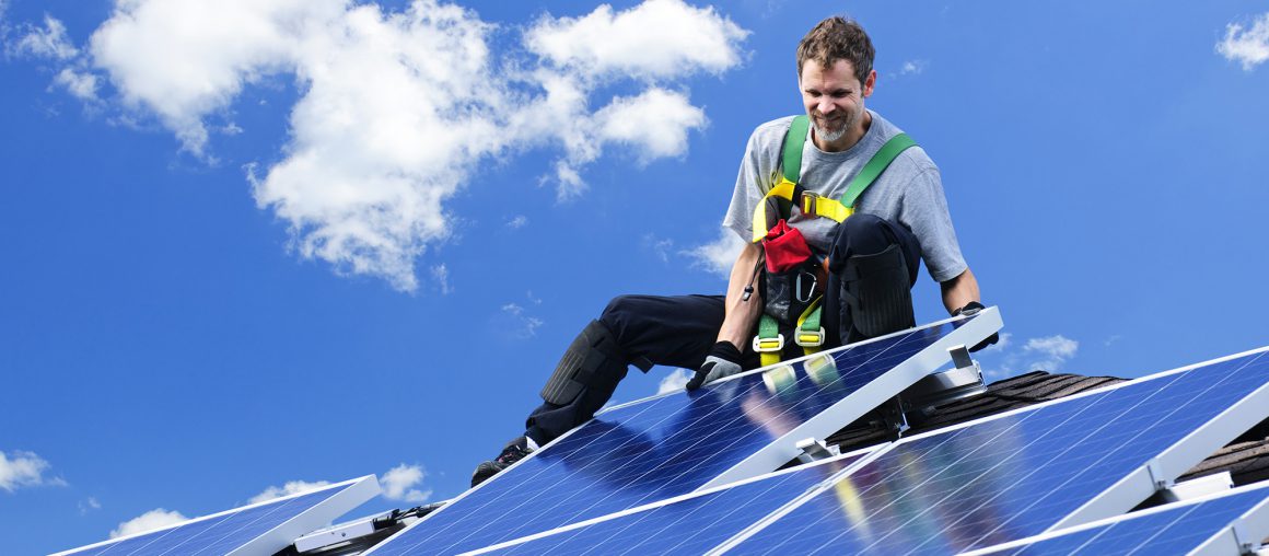 Worker installing alternative energy photovoltaic solar panels on roof
