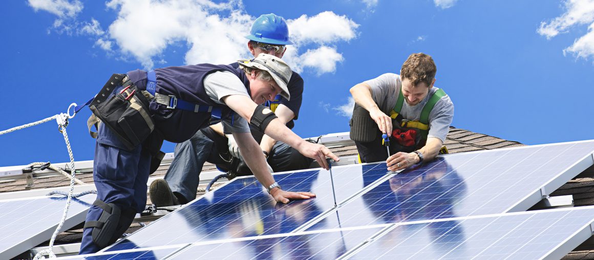 Workers installing alternative energy photovoltaic solar panels on roof